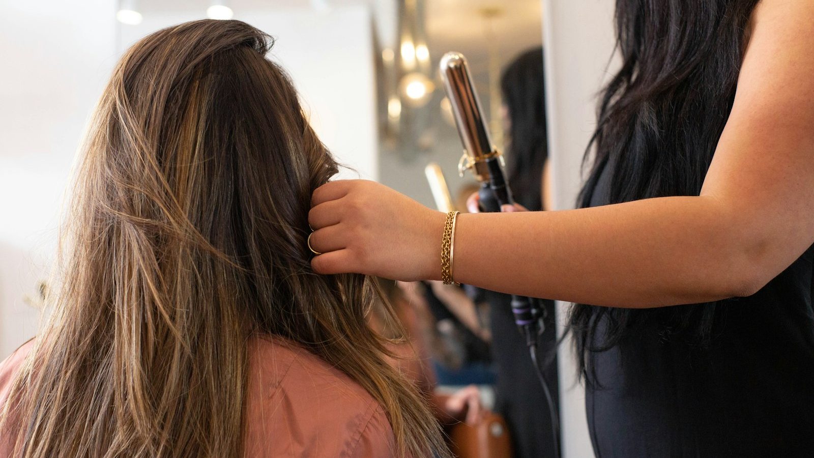 Hair salon near me within 400m open now: stylist curling a client's long hair