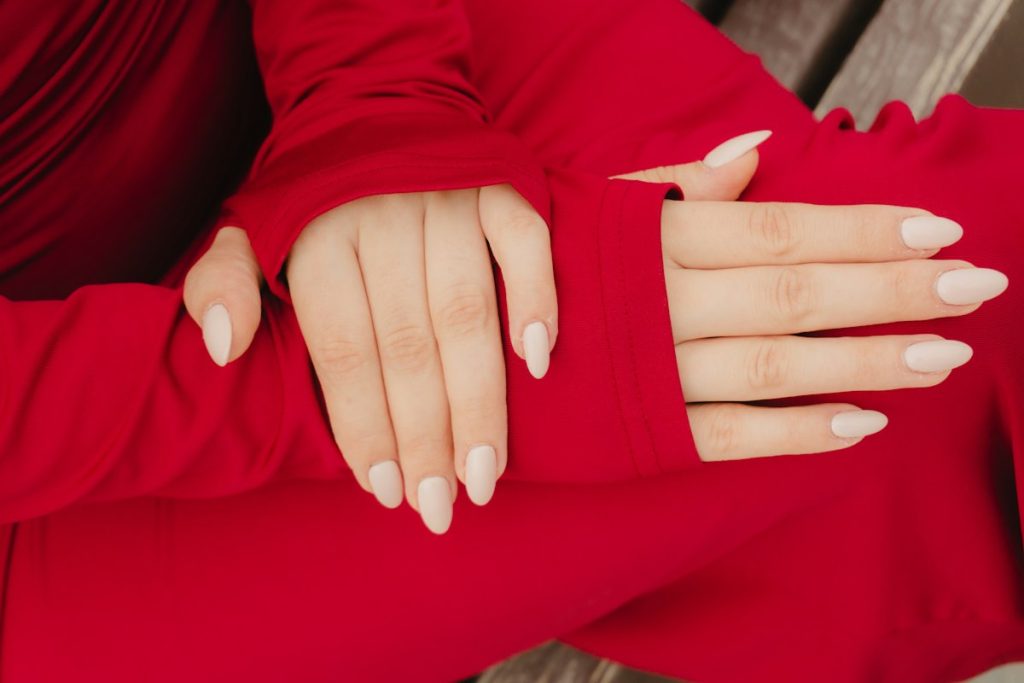 Nail design: milky almond nails against a red sleeve