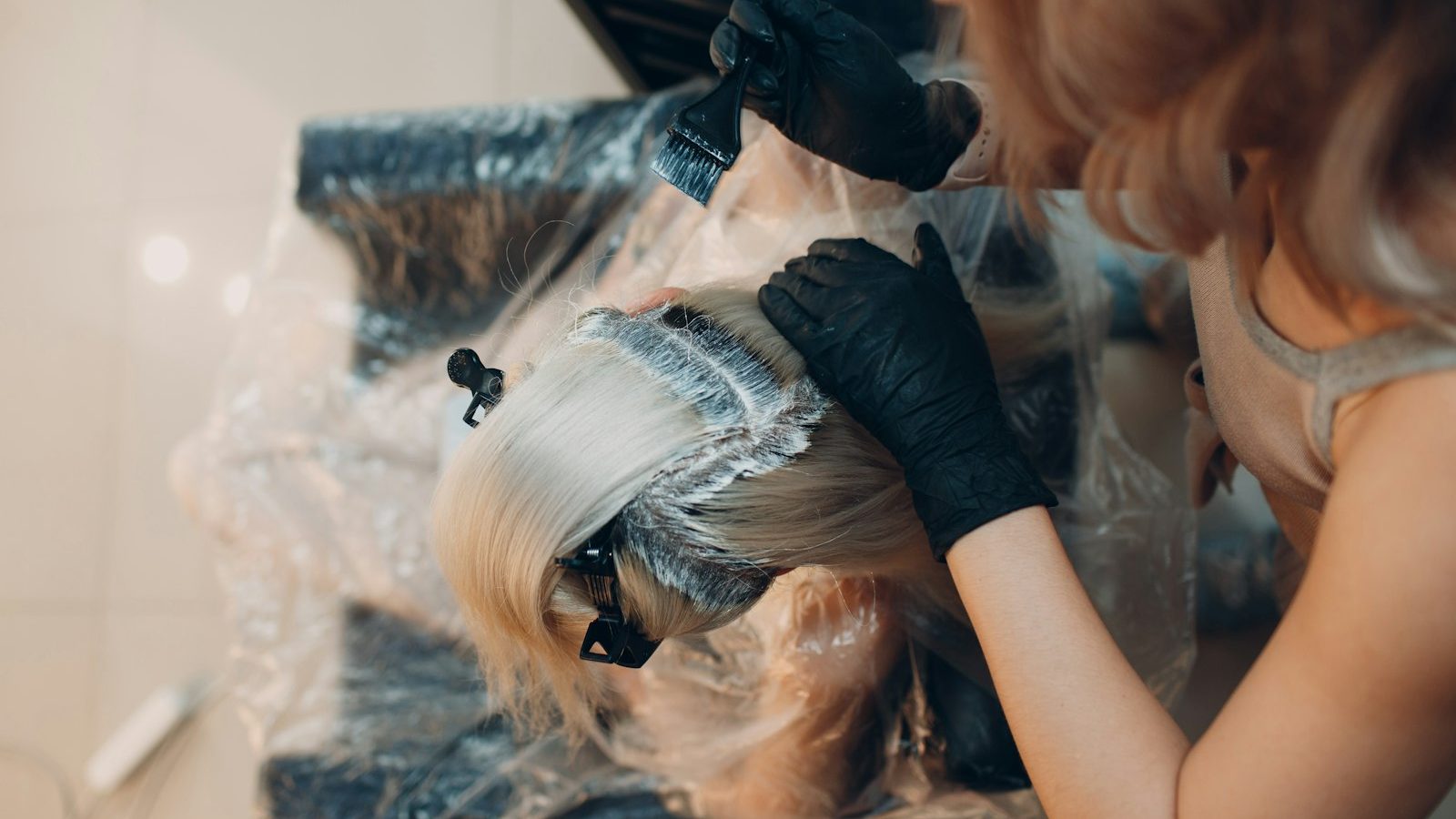 Hair after bleaching: colourist lightening blonde hair with gloves on