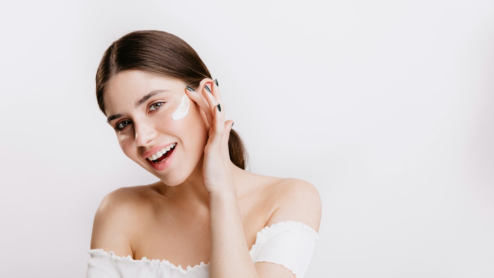 Dry skin: smiling woman applying moisturiser to her cheek