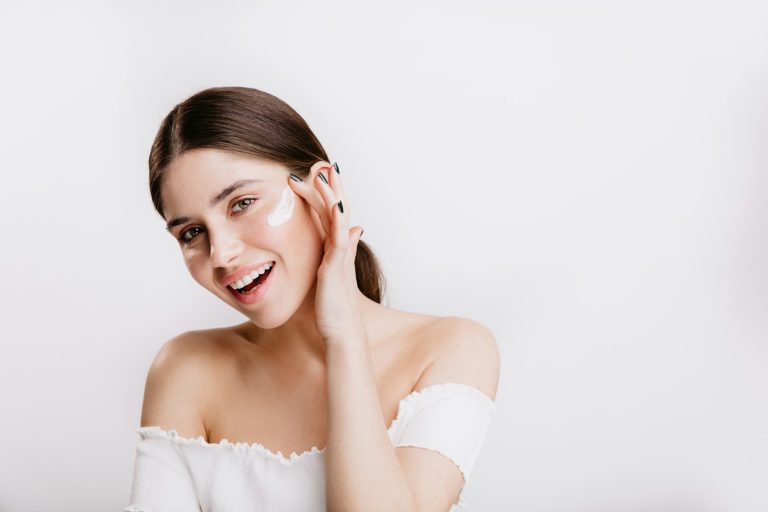Dry skin: smiling woman applying moisturiser to her cheek