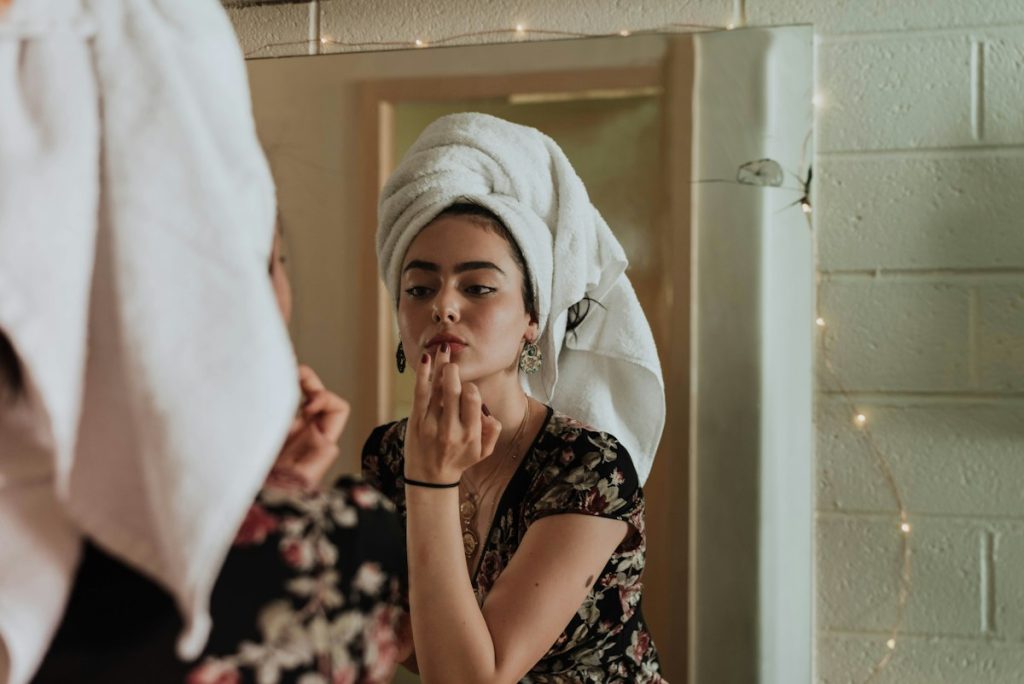 Dry skin: woman in a hair towel doing her skincare at the mirror